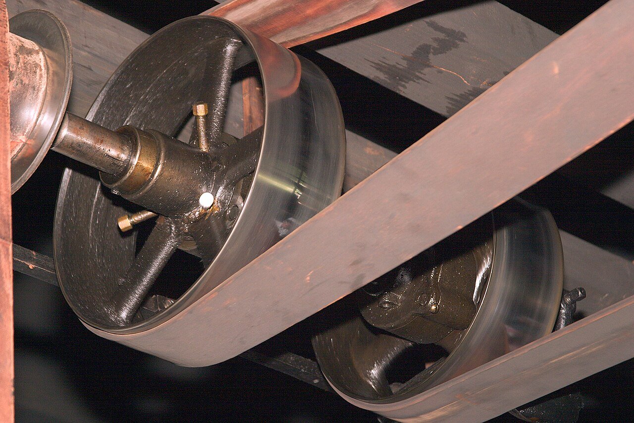 Flat belt drive in a machine shop — check belt speed before any RPM increase.