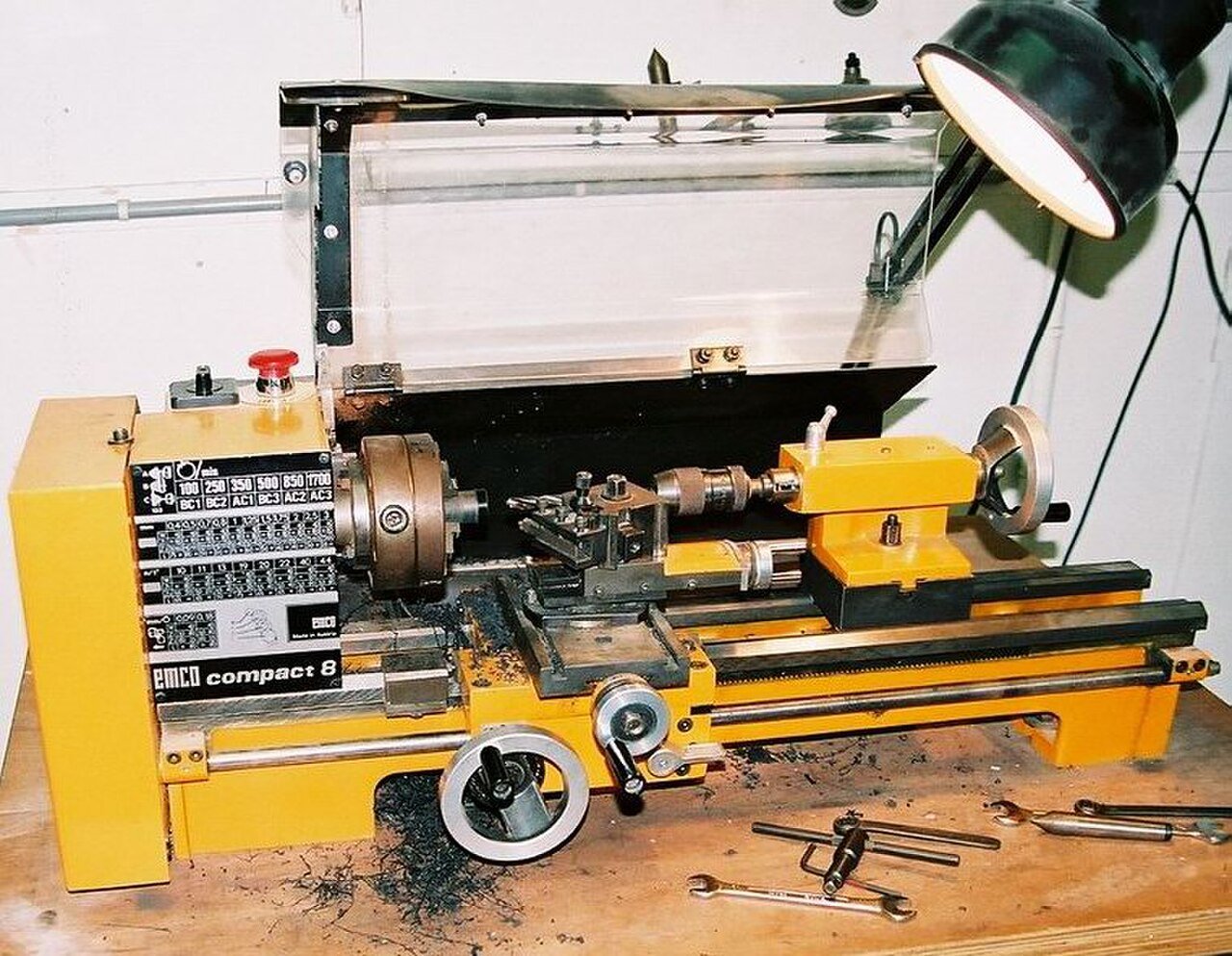 Bench lathe in a workshop with a belt-speed chart plate showing spindle speeds from 100 to 1,700 RPM