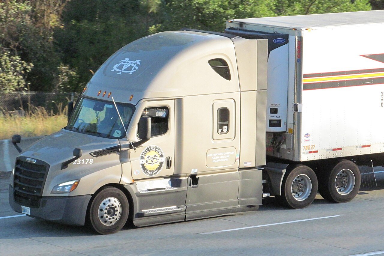 A Freightliner semi-truck with a refrigerated trailer on Interstate 90 — trucks live at much higher lb/hp than cars